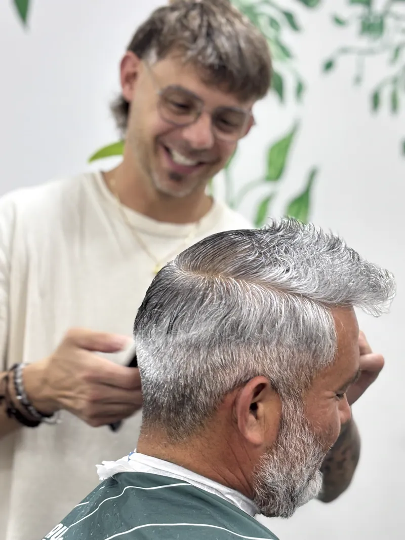 Peluquero con anteojos sonriendo mientras trabaja con una máquina