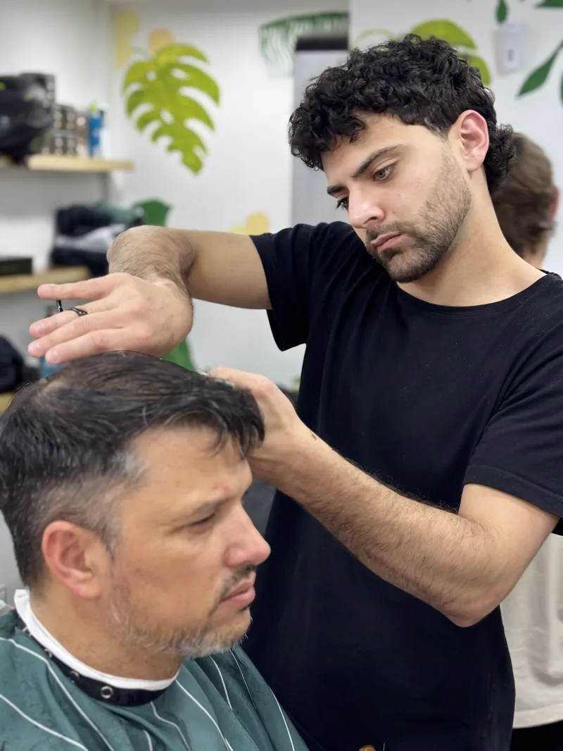 Peluquero de pelo rizado trabajando junto a un mural de plantas