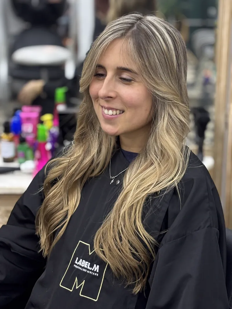 Clienta sonriendo con cabello largo y mechas rubias